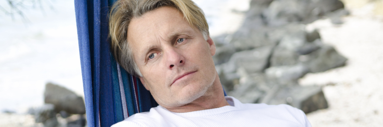 Still Struggling With Fibromyalgia Symptoms on Vacation man lying in a hammock on the beach looking upset and pensive