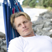 man lying in a hammock on the beach looking upset and pensive