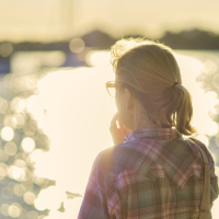 woman in a plaid shirt with a blonde ponytail looking at the reflection of light on a lake