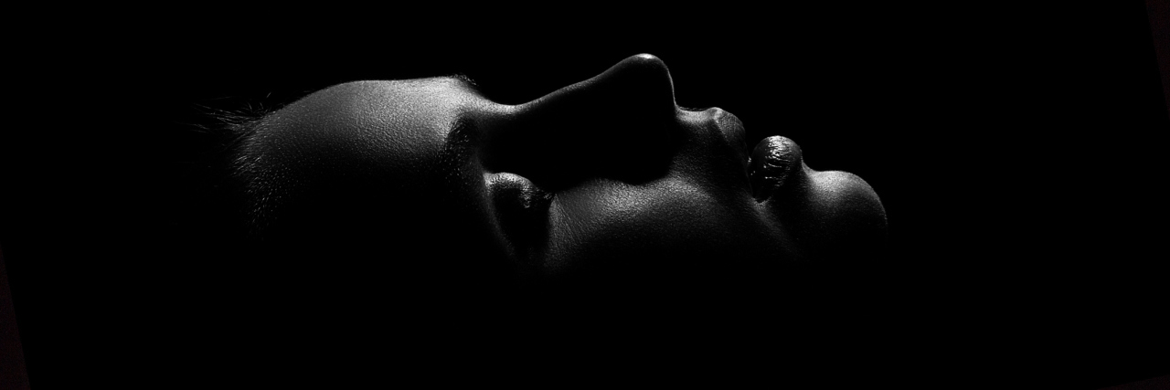 black and white portrait of a woman lying down with her eyes closed in the dark