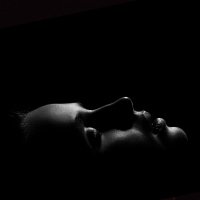 black and white portrait of a woman lying down with her eyes closed in the dark