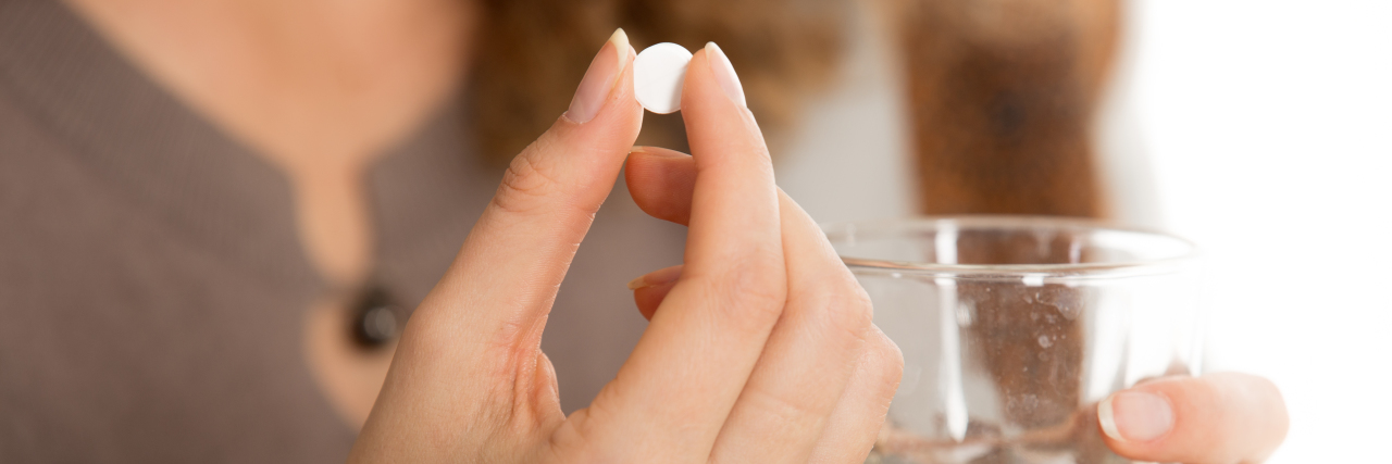 Female hands hold one pill and glass of water close-up