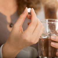 Female hands hold one pill and glass of water close-up