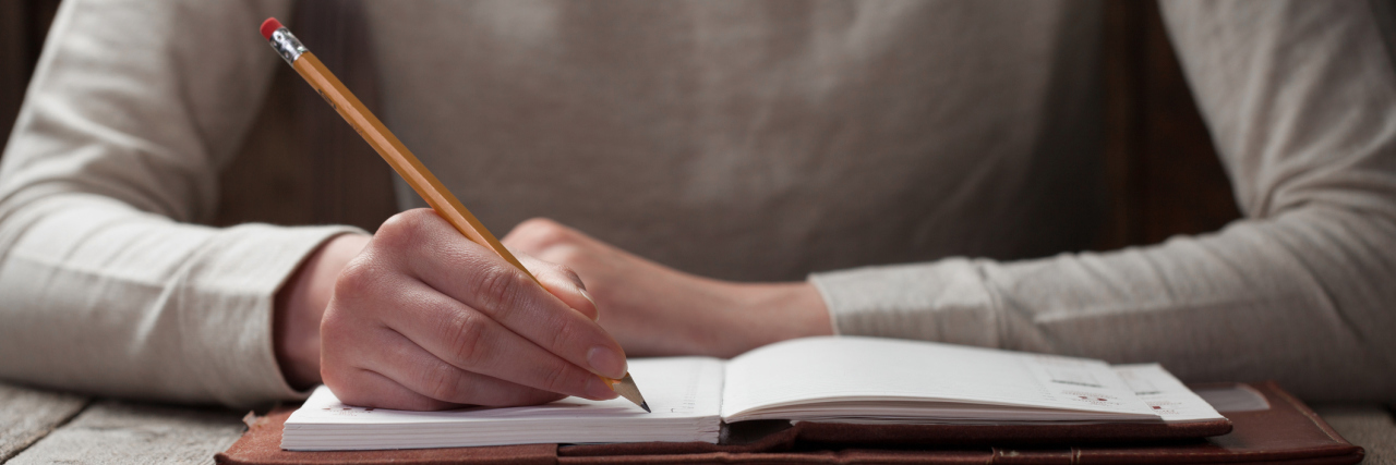 A woman writing with a pencil in a journal.