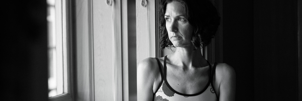Accepting My Auditory Hallucinations Were Schizoaffective Disorder black and white photo of middle aged woman sitting on windowsill looking out