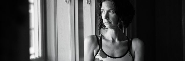 black and white photo of middle aged woman sitting on windowsill looking out
