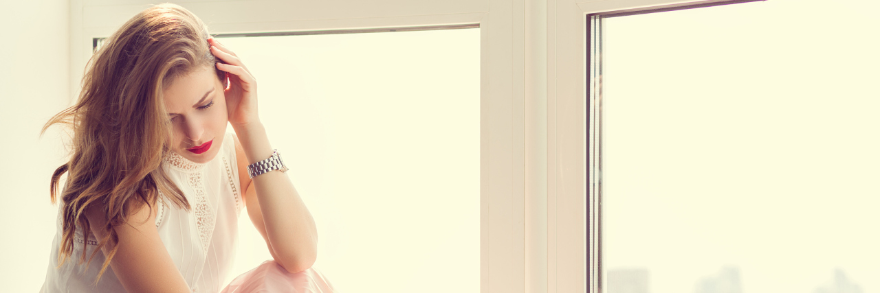 A woman with a serious expression sitting by a window.