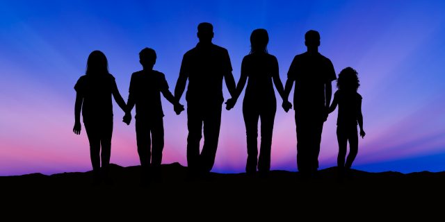 Silhouette of a family comprising a father, mother and children walking into the sunset