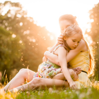 Mother holding daughter in bright sunlight meadow