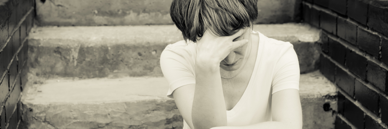 A woman sits on the concrete stairs in a very depressed mood, lying next to her on the stairs of her backpack.