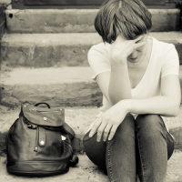 A woman sits on the concrete stairs in a very depressed mood, lying next to her on the stairs of her backpack.