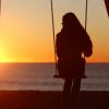 Woman on a swing at the beach at sunset,
