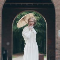 Victorian fashion girl with umbrella standing in front of gate.