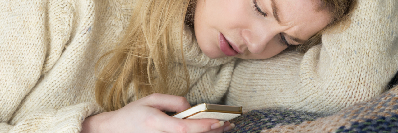 How I Ask for Help When My Depression Takes Control young blonde woman looking upset with smartphone in hand and head on arm