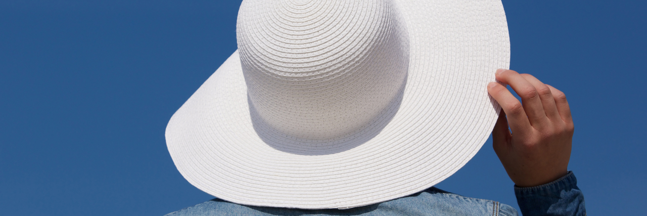 Advice for Living With Solar Urticaria Close up portrait of the back of a young woman with white sun hat from behind