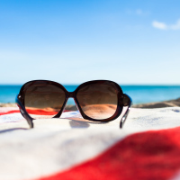sunglasses sitting on a red and white striped towel on the beach