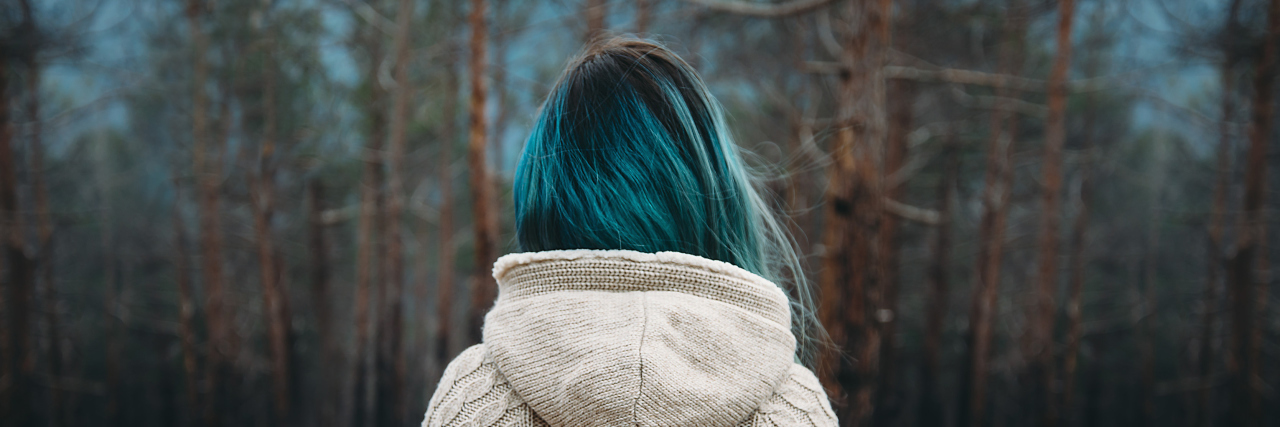 Feeling Like I Can't Be Myself Due to Ehlers-Danlos Syndrome woman with blue hair wearing a white sweater and standing in front of a pine forest