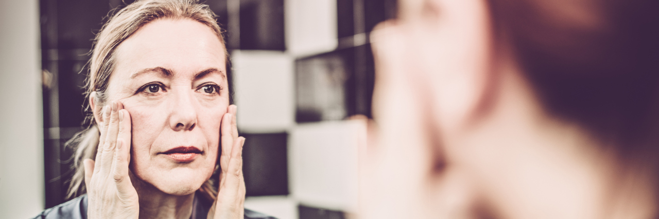 5 Ways I've Had to Adjust My Attitude Since My Diagnosis A woman touching her face and looking in the mirror at her reflection.