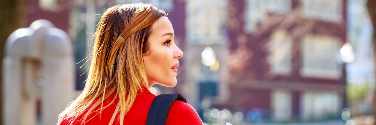 Why College Students With Chronic Illness Are Under Lots of Pressure college student wearing a red jacket and backpack and walking on campus