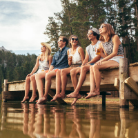 group of friends sitting on the edge of a dock on a lake