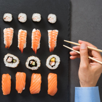 A picture of a man with a plate of sushi in front of him.