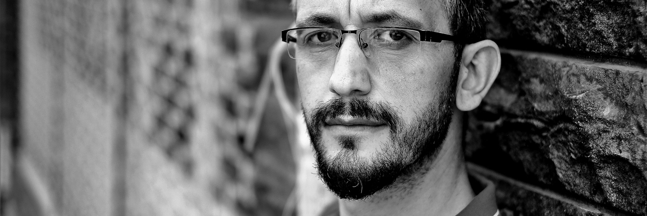 Why I Hide My Anxiety as an Adult Man black and white portrait of stoic man looking at camera leaning against wall