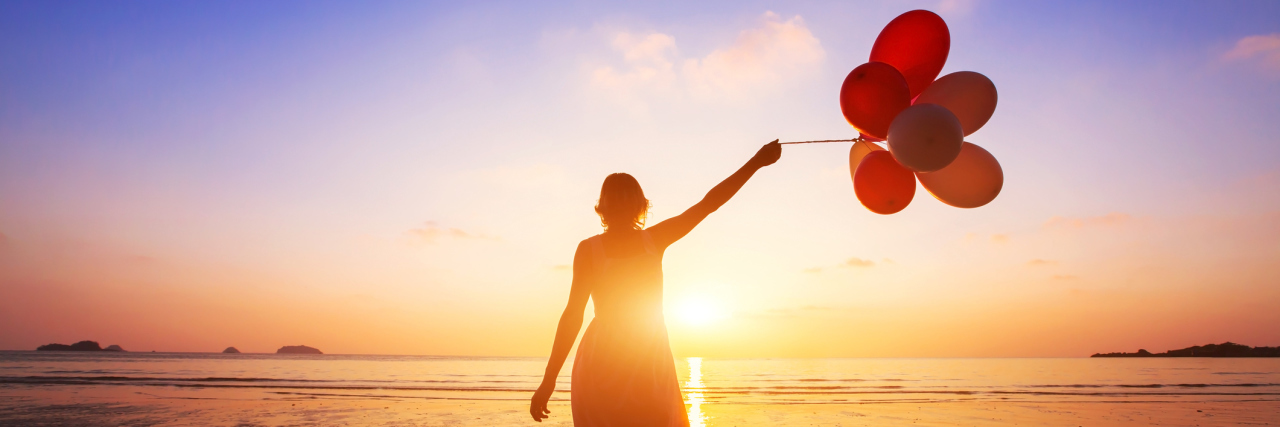 How Chronic Illness Taught Me to Slow Down to Reach My Goals A woman walking during a sunset, holding balloons.