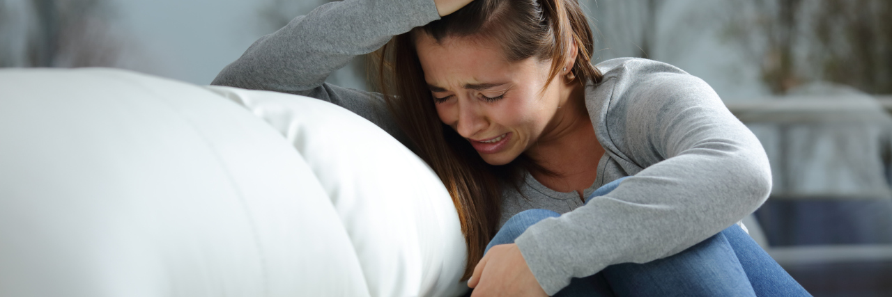 Remembering to Cry and Release Your Emotions With Chronic Illness woman sitting on her couch holding her knees to her chest and crying