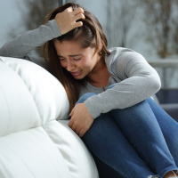 woman sitting on her couch holding her knees to her chest and crying