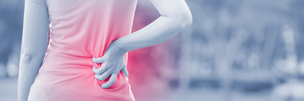 The Issue With The London Times' Article About Back Pain and Laziness woman walking in the park and holding her lower back in pain