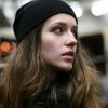 woman with long brown hair wearing a beanie and looking away on a train