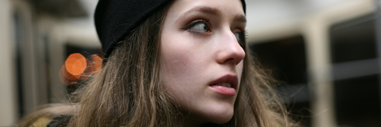 woman with long brown hair wearing a beanie and looking away on a train