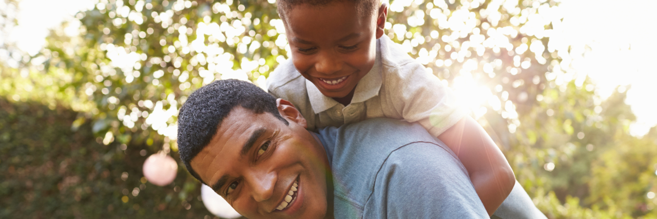 Young black boy playing on dad's back in a garden