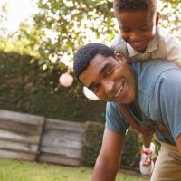 Young black boy playing on dad's back in a garden