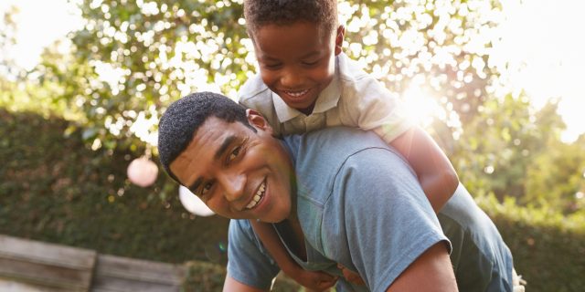 My Question About 'Autism Uncensored' as an Autistic Dad Young black boy playing on dad's back in a garden