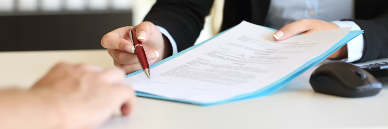 Why Cancellation Policies Are Hard for People With Chronic Illness Close up of an executive hands holding a pen and indicating where to sign a contract at office