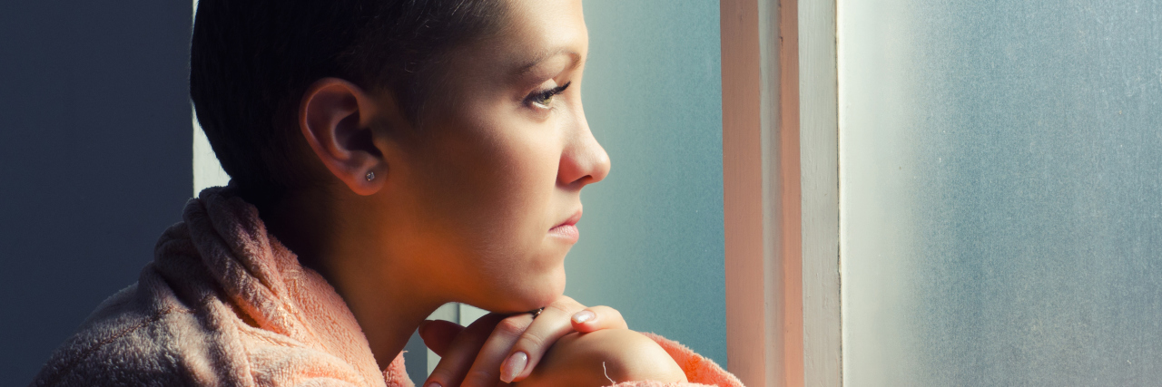 Young cancer patient standing in front of hospital window