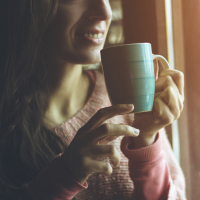 woman standing by a window and drinking coffee from a blue mug