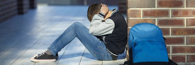 young schoolboy crying in hallway on floor at school