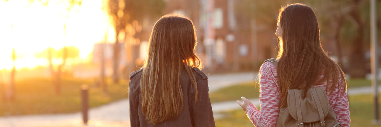 4 Things Not to Say to Someone With a Digestive Disease Back view of two friends walking together in a park at sunrise with a warm light in the background