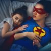 mother lying in bed with two small children sleeping on either side of her. the mom is wearing a superhero costume