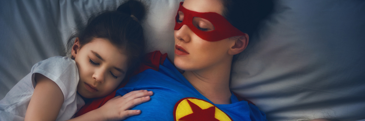 mother lying in bed with two small children sleeping on either side of her. the mom is wearing a superhero costume