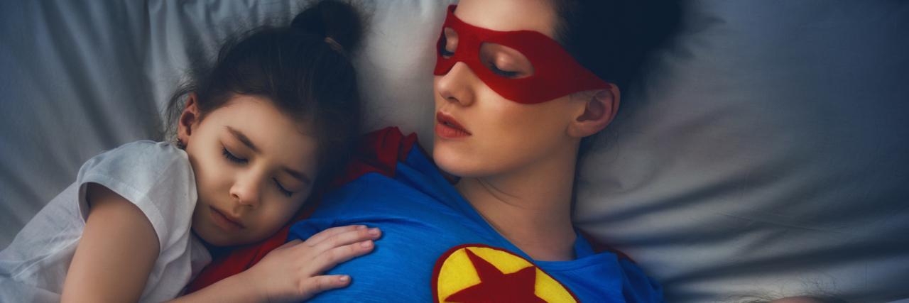 Why Parents With Chronic Illnesses Are Superheroes mother lying in bed with two small children sleeping on either side of her. the mom is wearing a superhero costume