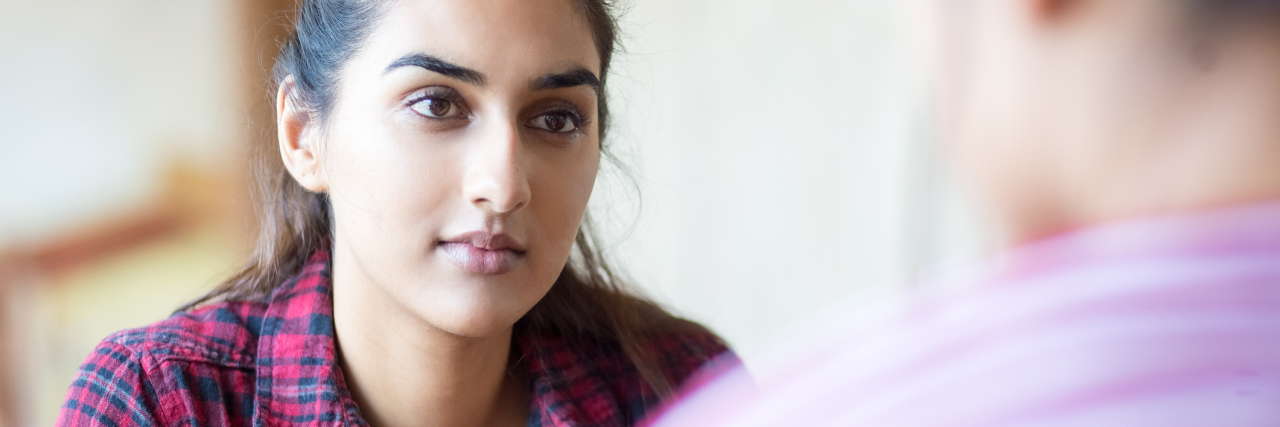 woman in pink and blue plaid shirt talking to a male friend