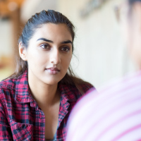 woman in pink and blue plaid shirt talking to a male friend
