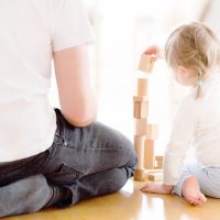 Cute girl playing with wooden blocks ont he floor with her father