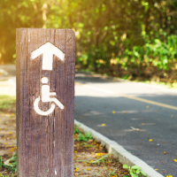 Disability sign with arrow pointing towards trail.