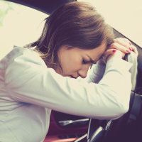 tired woman in car leaning against steering wheel