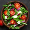 Fresh salad with arugula, feta cheese, red onion and red currant in a bowl.