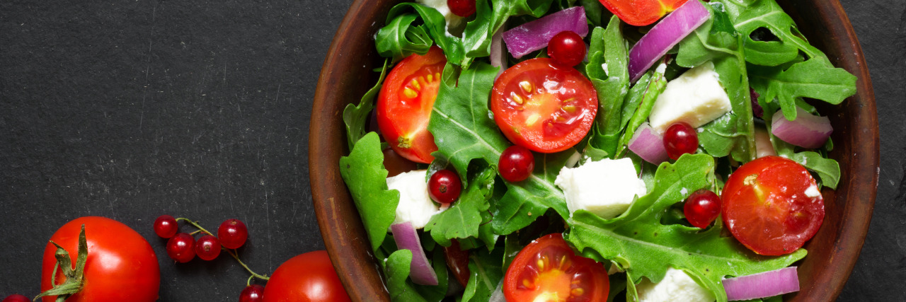 Fresh salad with arugula, feta cheese, red onion and red currant in a bowl.